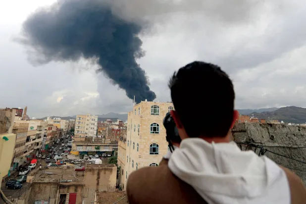 مصور صحافي يلتقط من سطح بناية في صنعاء صورة لموقع استهدفته ضربة إسرائيلية أمس (أ.ف.ب)