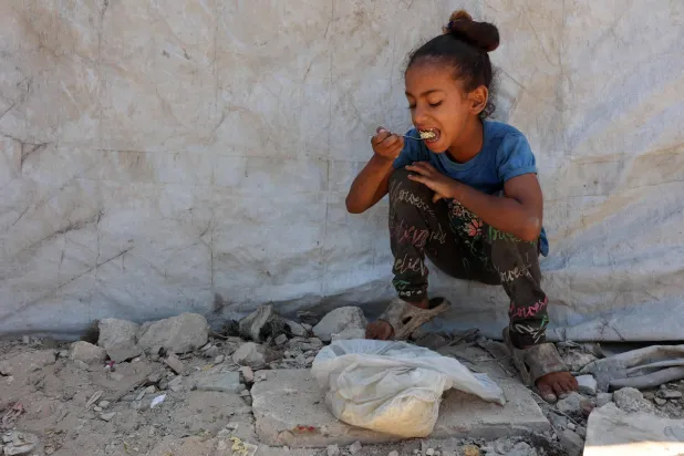 دختر فلسطینی دیروز در شهر غزه برنج پخته‌ای را که از یک آشپزخانه خیریه گرفته بود، می‌خورد (AFP)