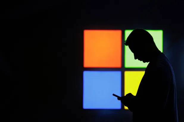 شخص يستخدم هاتفه أمام شعار «مايكروسوفت» (رويترز)