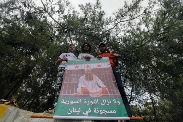شباب يحملون صورة الشيخ المتشدد أحمد الأسير المعروف بمواقفه ضد «حزب الله» والمحكوم بالسجن على خلفية الاشتباك مع عناصر الجيش في صيدا عام 2013، وكتب على الصورة «لا تزال الثورة السورية مسجونة في لبنان» (إ.ب.أ)