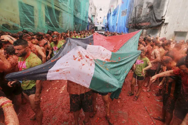 أشخاص يحملون العلم الفلسطيني خلال مهرجان الطماطم في إسبانيا (أ.ب)