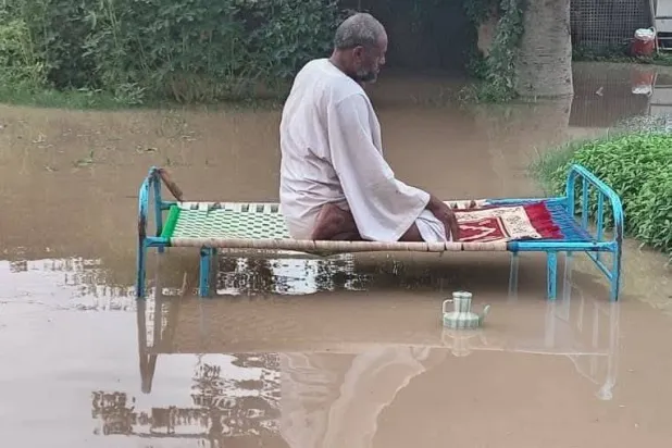 مواطن يؤدي الصلاة على سرير وسط المياه في الخرطوم (فيسبوك)