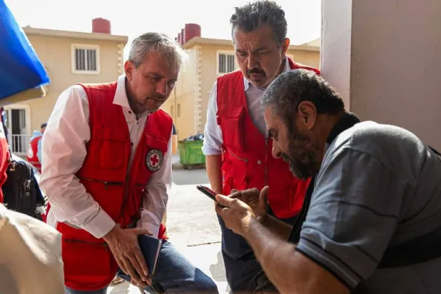 رئيس بعثة الصليب الأحمر الدولية ستيفان ساكاليان يشاهد صورة أحد المفقودين على هاتف أحد أقاربه في مركز إيواء بريف دمشق (الصليب الأحمر)