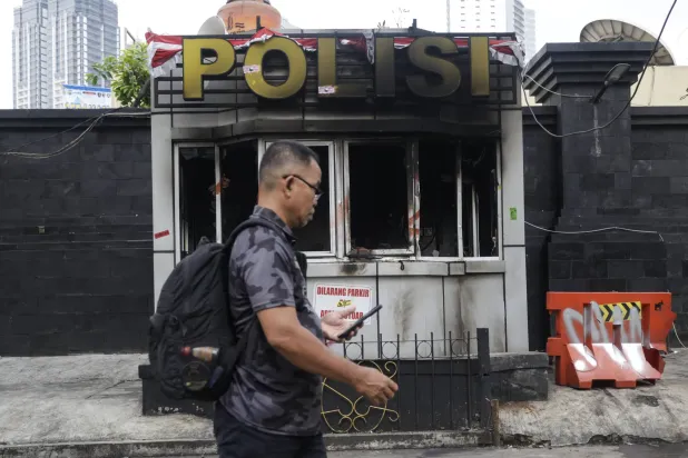 رجل إندونيسي يمر أمام نقطة شرطة محترقة في العاصمة الإندونيسية جاكارتا (إ.ب.أ)