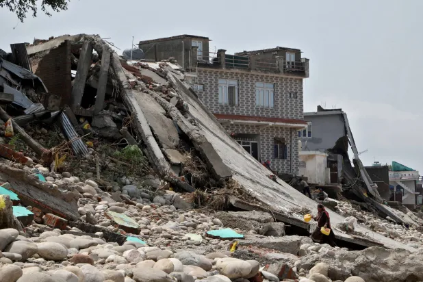 امرأة تحمل عبوات بلاستيكية عثرت عليها في ركام منزلها الذي ضربته السيول في جامو (رويترز)