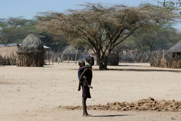 طفلة متضررة من الجفاف المتفاقم بسبب فشل مواسم الرياح الموسمية تحمل شقيقها داخل قرية سوبيل في توركانا كينيا (رويترز)