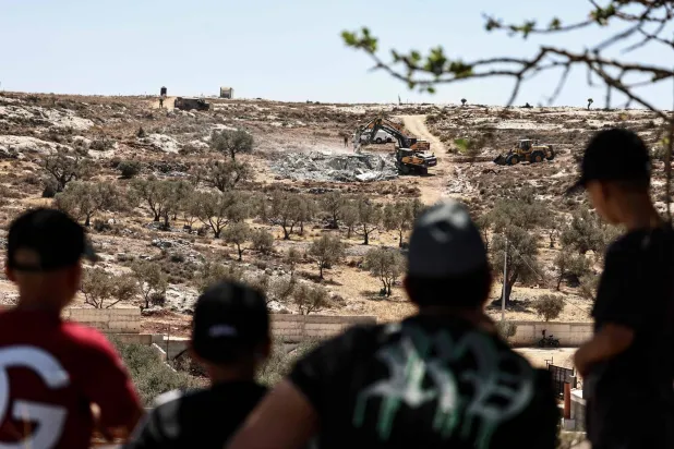 شباب فلسطينيون يشاهدون آليات تابعة لجيش الاحتلال الإسرائيلي تهدم منازل فلسطينيين في إحدى قرى رام الله بالضفة الغربية المحتلة قبل يومين (أ.ف.ب)