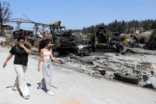 لبنانيتان تسيران قرب موقع استهداف إسرائيلي لباحة صيانة جرافات في بلدة أنصارية بجنوب لبنان (إ.ب.أ)