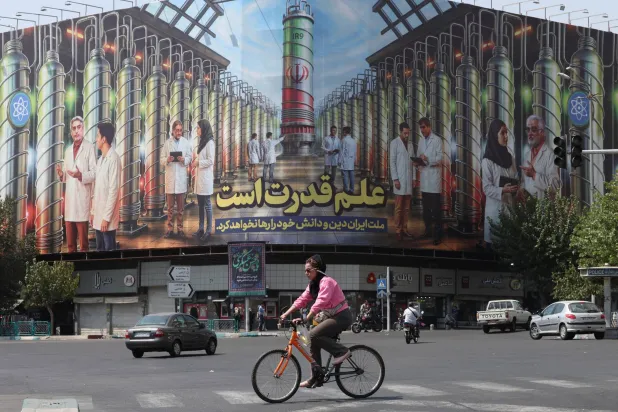 إيرانية تركب دراجة هوائية بجوار لوحة إعلانية تعرض صورة أجهزة الطرد المركزي النووية وجملة بالفارسية تقول «العلم هو القوة والأمة الإيرانية لن تتخلى عن دينها ومعرفتها» في ساحة الثورة بطهران (إ.ب.أ)