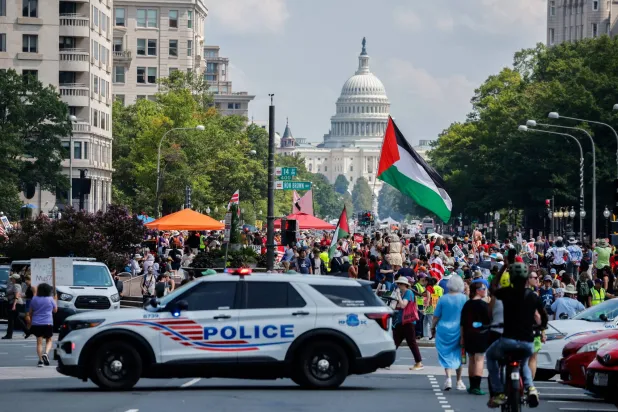 متظاهرون مناهضون لنشر الحرس الوطني في واشنطن بجوار سيارة شرطة قرب مبنى الكابيتول (رويترز)