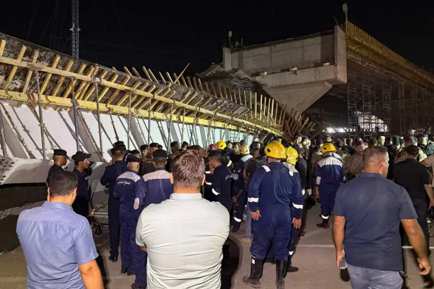 مسعفون ومارة يتجمعون أمام جسر قيد الإنشاء بعد انهيار جزء منه ما أدى إلى مقتل شخصين وإصابة آخرين في مدينة كربلاء جنوب العراق (أ.ف.ب)