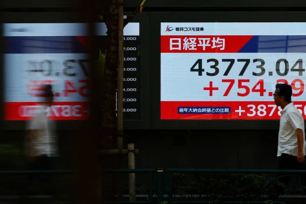 رجل يمر أمام شاشة تعرض حركة الأسهم في وسط العاصمة اليابانية طوكيو (رويترز)