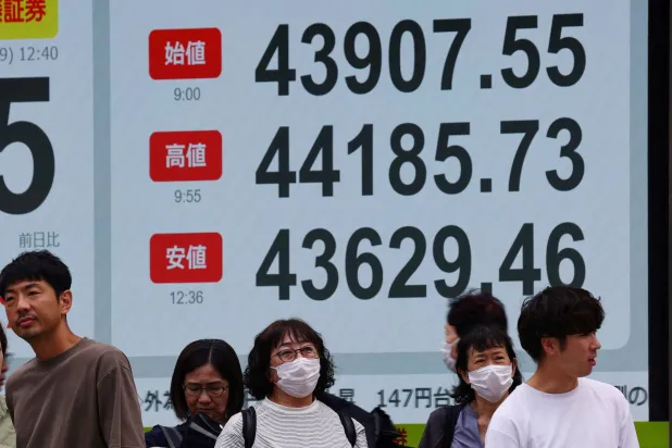 مشاة يمرُّون أمام شاشة تعرض حركة الأسهم وسط العاصمة اليابانية طوكيو (رويترز)