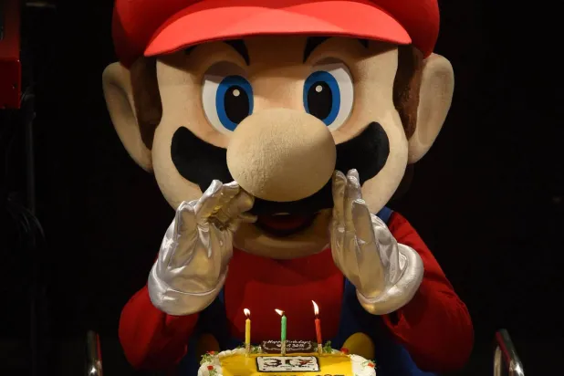 «سوبر ماريو» وهو يحاول إطفاء الشموع على كعكة خلال احتفالات وعرض حيٍّ لأشهر موسيقى ماريو بمناسبة الذكرى الثلاثين للعبة في طوكيو عام 2015 (أ.ف.ب)