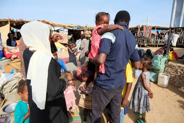 نازح سوداني يحتضن أبناء شقيقته التي قُتلت في الفاشر بعد لقائه بعائلته في أحد مخيمات النزوح بمدينة الدبة (رويترز)