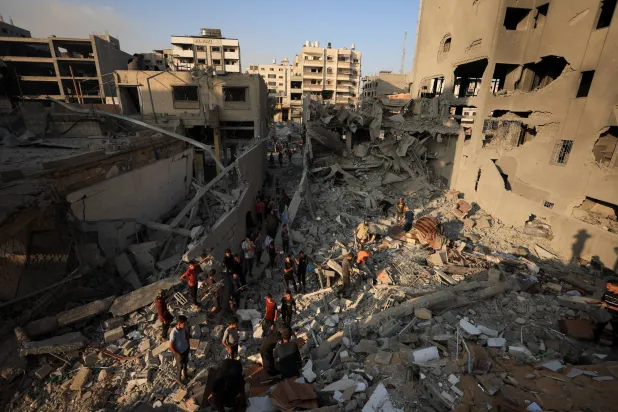 فلسطينيون يتفقدون الدمار في موقع الغارات الإسرائيلية التي دمرت برج الجندي المجهول السكني أمس الأحد بمدينة غزة (رويترز)