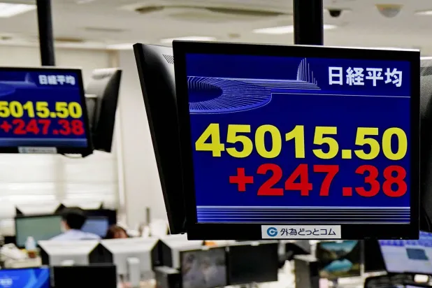 موظفو شركة تداول عملات أجنبية يجلسون تحت لوحة إلكترونية تعرض مؤشر «نيكي 225» الياباني (أ.ب)