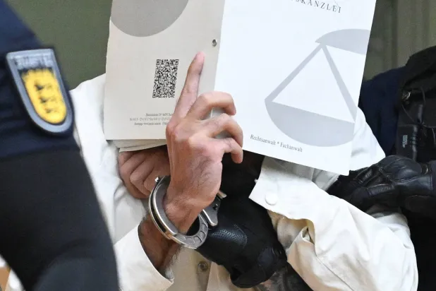 يصل المتهم سليمان وهو يغطي وجهه بملف إلى قاعة المحكمة الإقليمية العليا في شتوتغارت في 16 سبتمبر 2025 لحضور محاكمة بتهمة قتل ضابط شرطة وإصابة 5 آخرين أواخر مايو 2024 (رويترز)