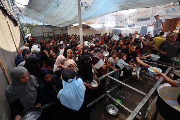 فلسطينيون يحملون أوانيهم أمام مطبخ خيري في مخيم النصيرات للاجئين وسط قطاع غزة 14 سبتمبر 2025 (أ.ف.ب)