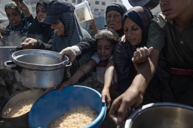 فلسطينيون بينهم أطفال يحملون الأواني أثناء انتظارهم للحصول على الطعام المجاني في مدينة غزة شمال القطاع (إ.ب.أ)