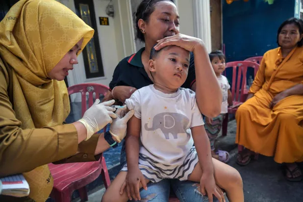 عاملة صحية تعطي لقاحاً ضد الحصبة لطفل في سورابايا بإندونيسيا (أ.ف.ب)