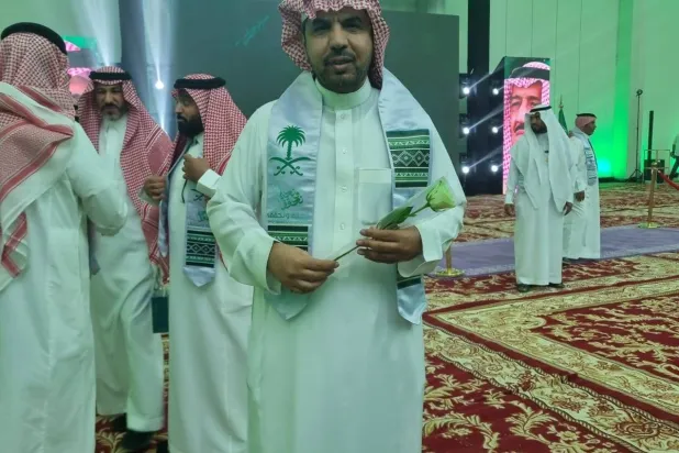 الدكتور عبد الرحمن الشقير متوشحاً شعار اليوم الوطني وحاملاً علم بلاده (الشرق الأوسط)