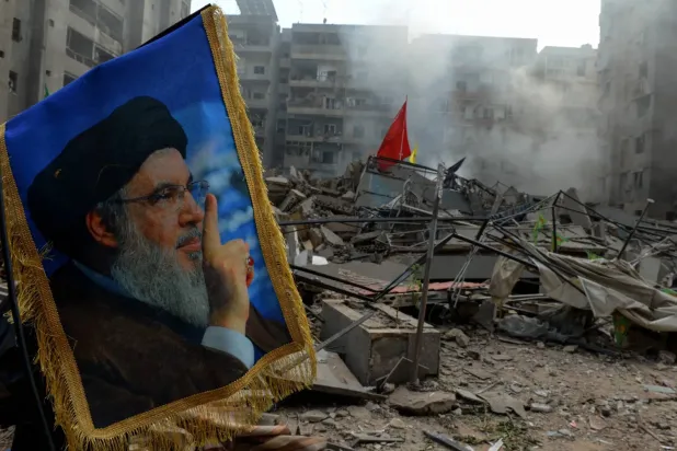Hasan Nasrallah'ın, Beyrut'un güney banliyölerinde İsrail uçaklarının yıktığı bir binanın enkazı önündeki fotoğrafı (DPA)
