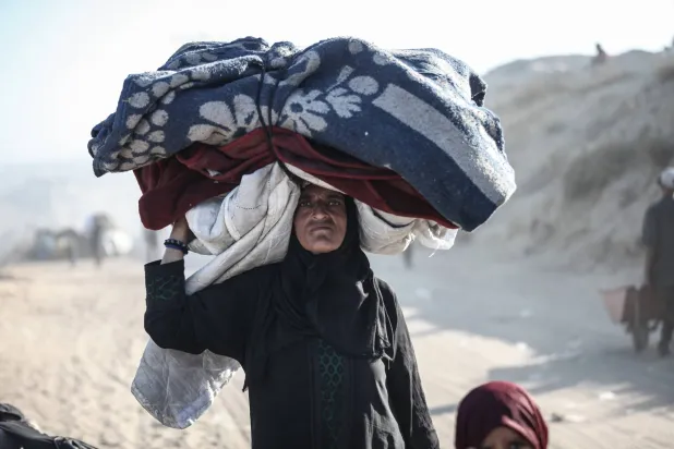 فلسطينية تحمل أمتعة على رأسها خلال النزوح سيراً على الأقدام في اتجاه جنوب قطاع غزة (د.ب.أ)