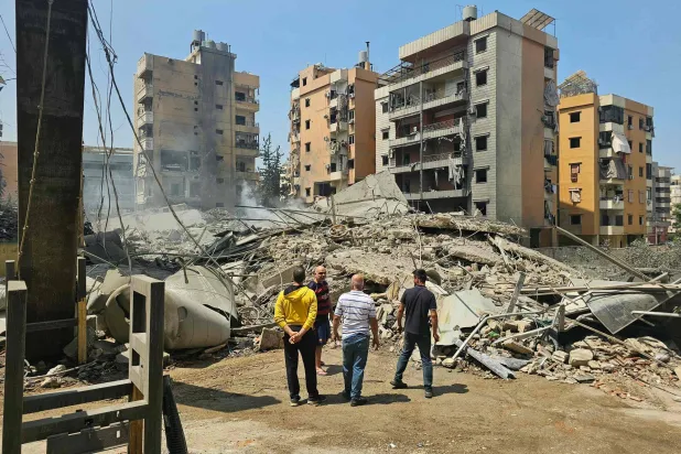 لبنانيون يقفون قبالة مبانٍ دمَّرتها غارات إسرائيلية استهدفت الضاحية الجنوبية لبيروت الأسبوع الماضي (أ.ف.ب)