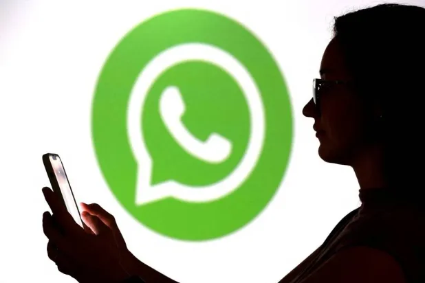 A teenager poses for a photo while holding a smartphone in front of a WhatsApp logo in this illustration taken September 11, 2025. (Reuters) 