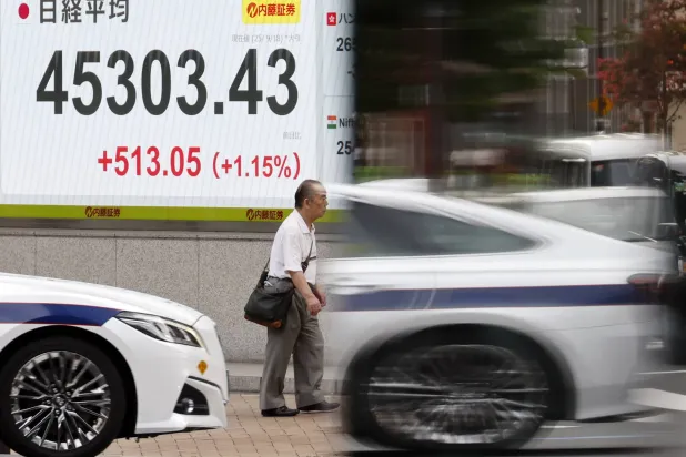 أحد المارة يسير أمام لوحة إلكترونية تعرض حركة الأسهم في شارع بالعاصمة اليابانية طوكيو (إ ب أ)