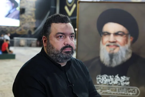 جواد نصر الله نجل الأمين العام السابق لـ«حزب الله» يتحدث في مقابلة وخلفه صورة والده حسن نصر الله (رويترز)