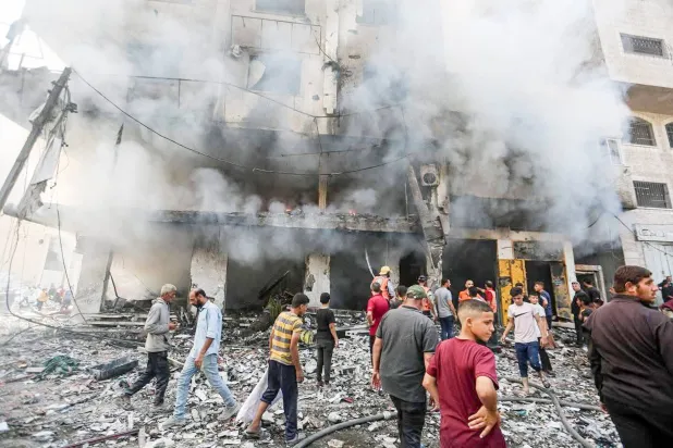 فلسطينيون خارج مبنى تضرر بغارة جوية إسرائيلية يوم الأحد (د.ب.أ)