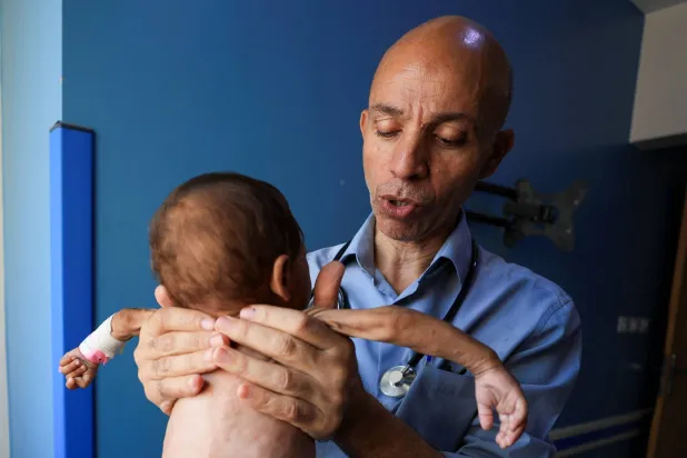 الطبيب أحمد بصل يحمل رضيعاً بدت ذراعاه نحيلتين من شدة الهزال بمستشفى الرنتيسي في غزة (رويترز)