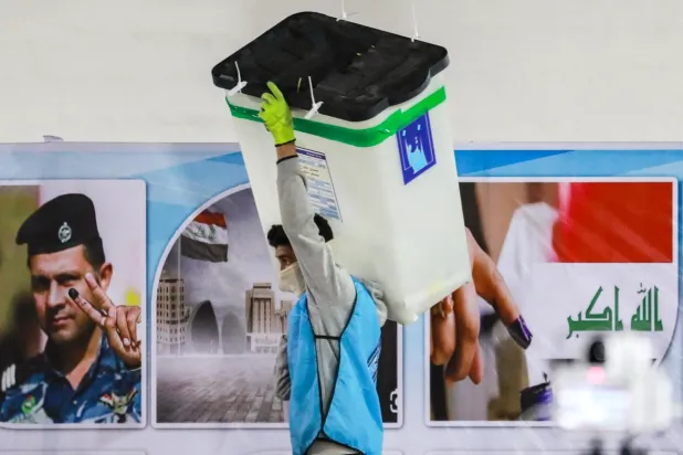 Irak Bağımsız Yüksek Seçim Komisyonu'nun çalışanı mühürlü bir oy sandığını taşırken, diğerleri Bağdat'ın Karh bölgesindeki Komisyonu'nun merkezlerinden birinde elektronik sayımla eşleşecek şekilde oyları elle sayıyor, 23 Aralık 2023 (AFP)