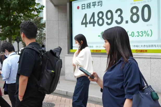 مشاة يسيرون أمام لوحة إلكترونية تعرض حركة الأسهم في وسط العاصمة اليابانية طوكيو (أ.ب)