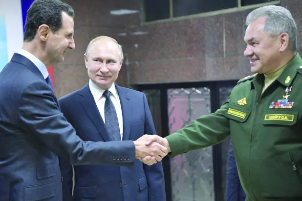الرئيس بوتين ينظر إلى الأسد وهو يصافح وزير الدفاع الروسي سيرغي شويغو في دمشق عام 2020 (أ.ف.ب)