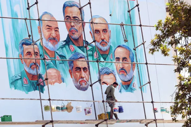 رسام يرسم لوحة على مبنى «مركز الإعلام الفلسطيني» في طهران تصور قادة عسكريين كباراً قتلوا في ضربة إسرائيلية (إ.ب.أ)