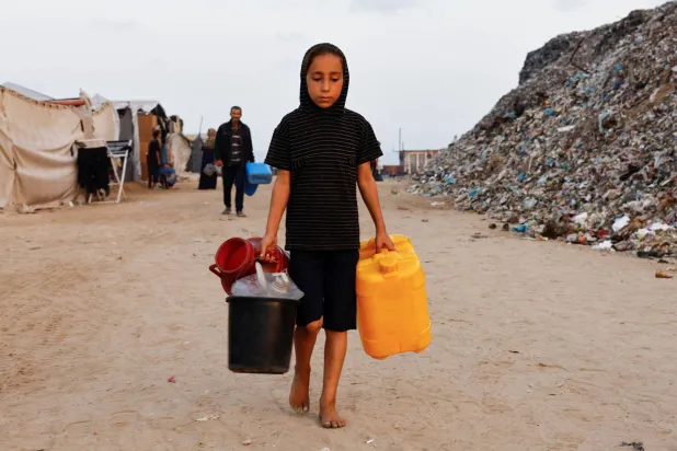 نازحة فلسطينية تحمل الماء في غزة (رويترز)