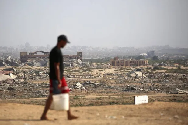A Palestinian man transports buckets of water next to a coastal path northwest of Nuseirat refugee camp after being displaced southward following an Israeli announcement of closing Al-Rashid road towards the north of the besieged Gaza Strip on October 4, 2025. (AFP)