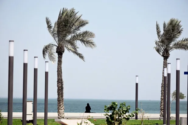 امرأة تجلس أمام مياه الخليج على ممشى بحري جرى تجديده مؤخراً بمنطقة الشويخ الساحلية بمدينة الكويت (أ.ف.ب)