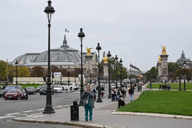 المارة يتجولون على إسبلاناد دي إينفاليد مع إطلالة على جسر ألكسندر الثالث والغراند باليه في باريس (أ.ف.ب)