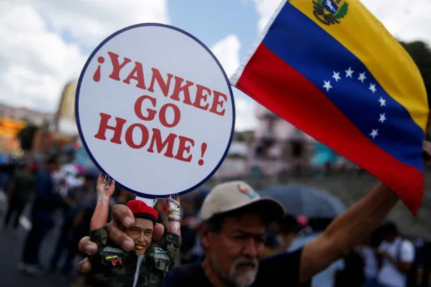 مؤيد للحكومة يحمل دمية تصور الرئيس الفنزويلي الراحل هوغو تشافيز مع لافتة كتب عليها: «أيها اليانكي عد إلى ديارك» خلال تجمعٍ لدعم الرئيس الفنزويلي نيكولاس مادورو في كراكاس (أ.ف.ب)