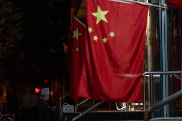 امرأة مسنة تقف بالقرب من الأعلام الوطنية الصينية المعلقة بمناسبة عطلة العيد الوطني (أ.ب)