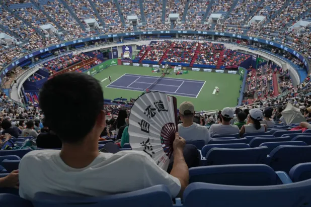 مشجع يبرّد نفسه بمروحة وهو يتابع مباراة بيرغس وديالو ضمن دورة شنغهاي (أ.ب)