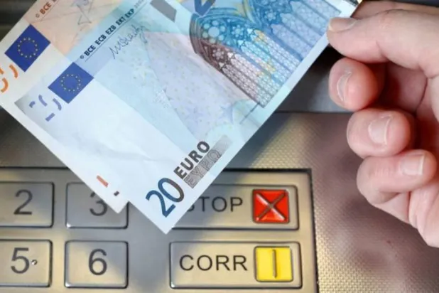 امرأة تمسك بأوراق نقدية من فئة 20 و50 يورو أمام صراف آلي في برن بألمانيا (رويترز)