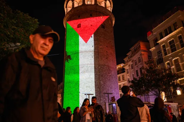 مشاة يمرون أمام برج غلاطة المضاء بالعلم الفلسطيني في إسطنبول أمس (أ.ف.ب)