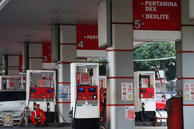 عامل يجلس مع بائع متجول أثناء انتظاره الزبائن بمحطة وقود تابعة لشركة بيرتامينا المملوكة للدولة في جاكرتا بإندونيسيا (رويترز)