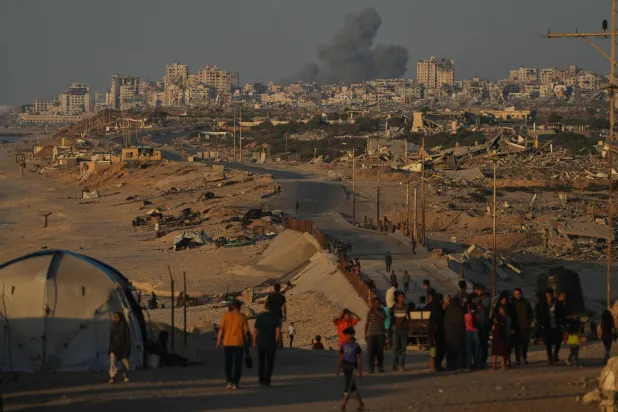 Displaced Palestinians walk along the coastal road, backdropped by smoke rising into the sky after an Israeli military strike in Gaza City, as seen from the central Gaza Strip, Wednesday, Oct. 8, 2025. (AP Photo/Abdel Kareem Hana)
