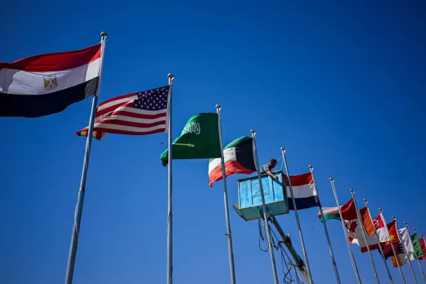 A municipal worker hoists flags of various countries near Sharm el-Sheikh International Airport ahead of the arrival of world leaders in Sharm el-Sheikh on October 11, 2025. (Photo by Khaled DESOUKI / AFP)